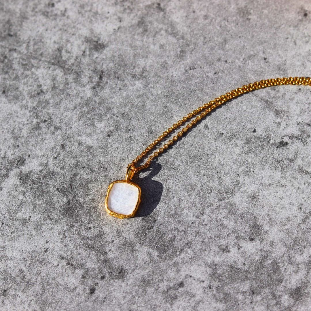 Photo of white stone gold plated necklace on a grey marble effect background.