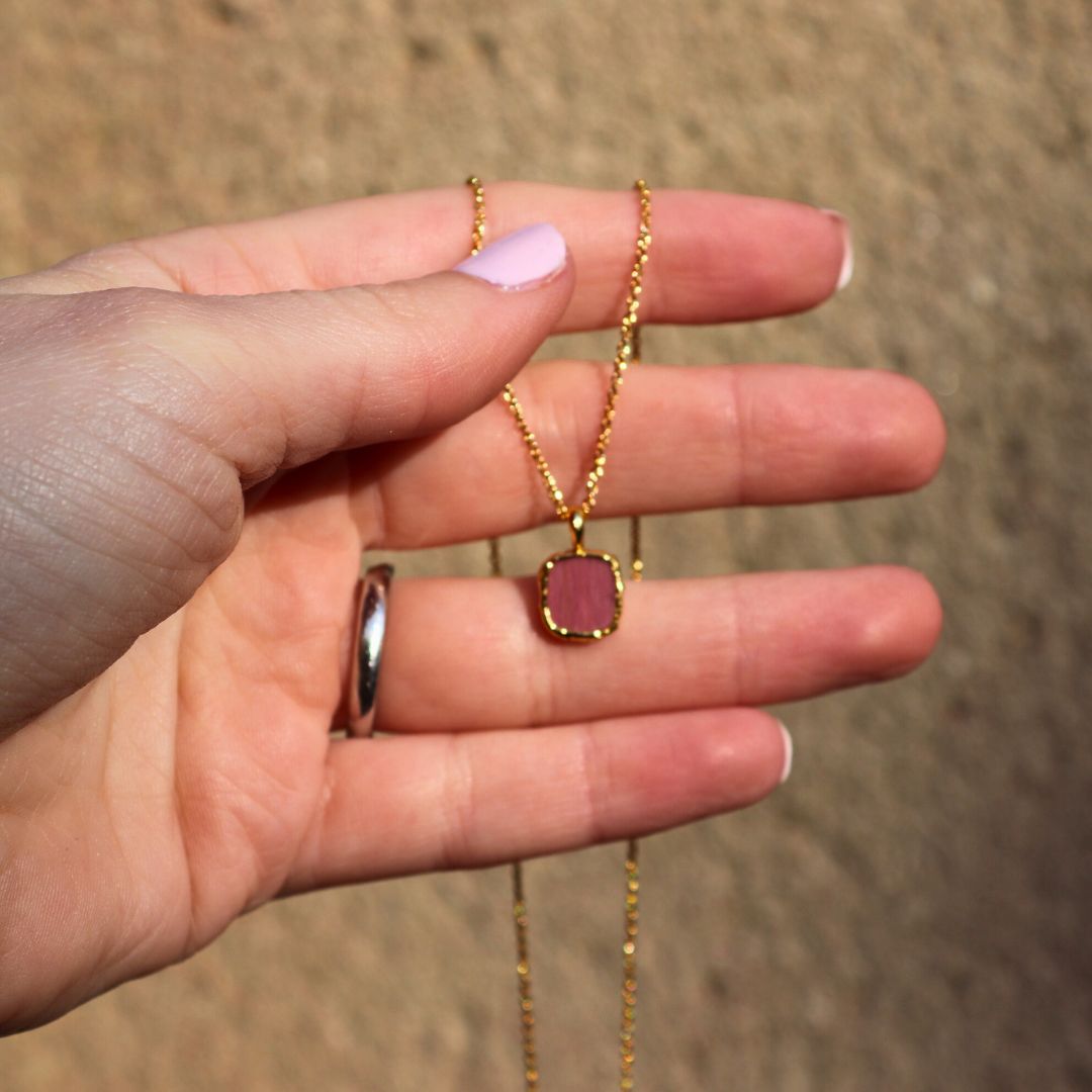 Photo of red stone gold plated necklace held in a females hand.