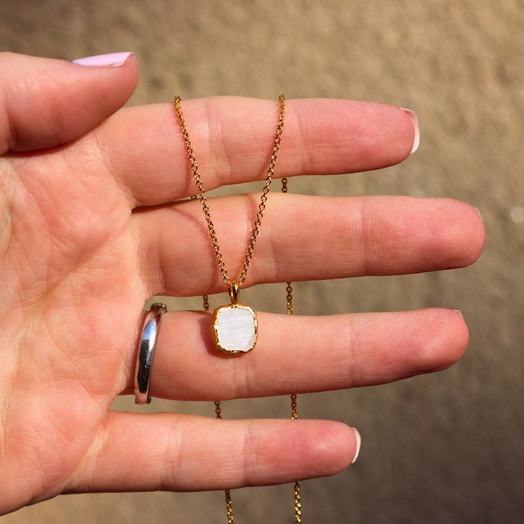 Photo of white stone gold plated necklace held in a females hand.