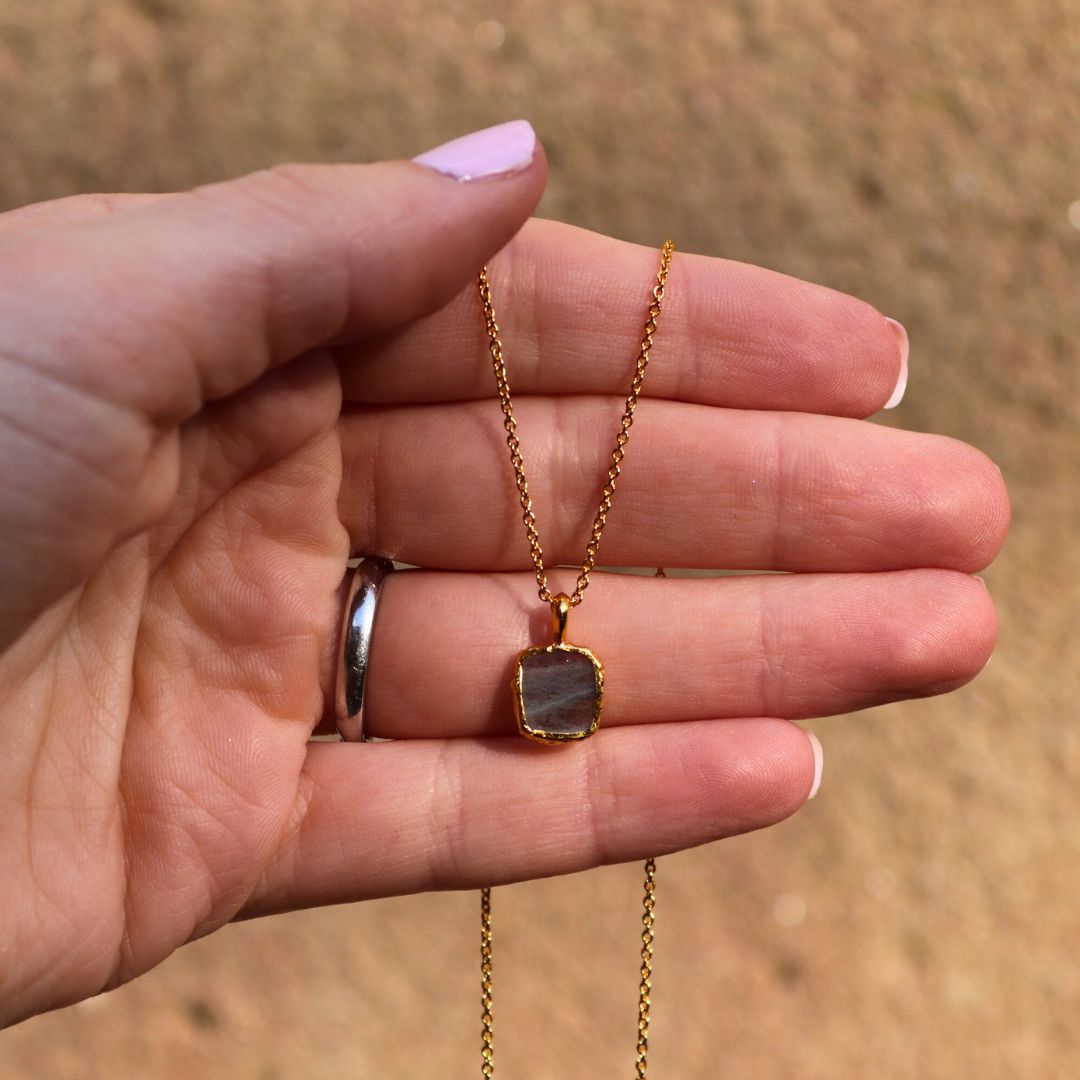 Photo of grey stone gold plated necklace held in a females hand.