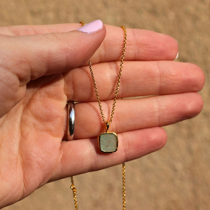 Photo of green stone gold plated necklace held in a females hand.