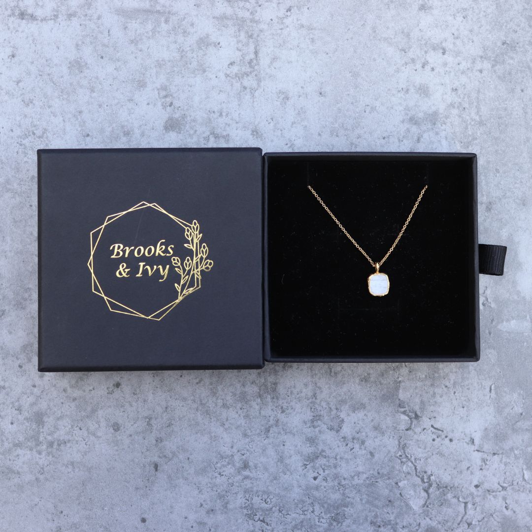 Photo of white stone gold plated necklace inside gift box on a grey marble effect background.