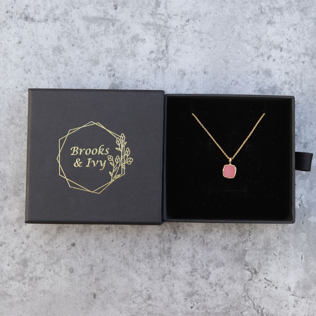 Photo of red stone gold plated necklace inside gift box on a grey marble effect background.