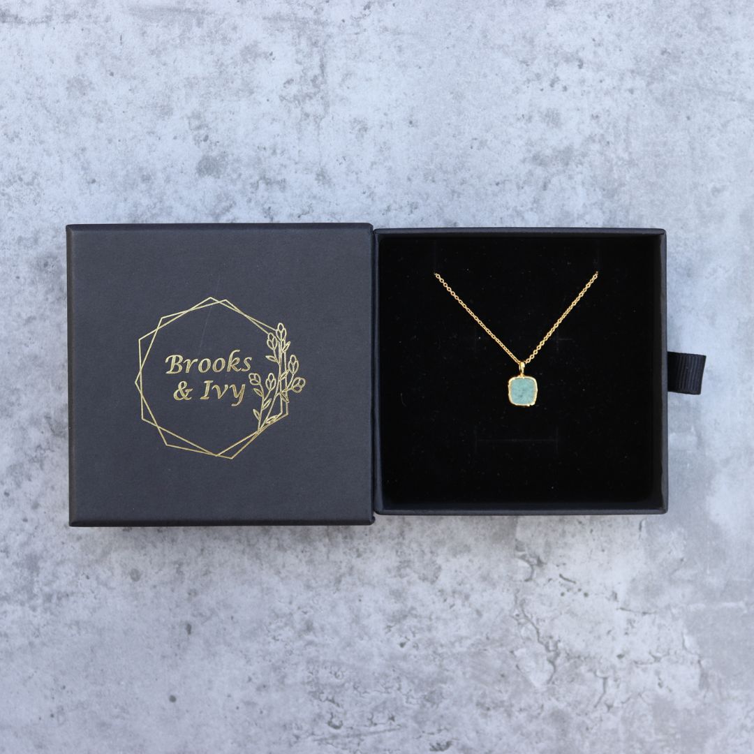 Photo of green stone gold plated necklace inside gift box on a grey marble effect background.