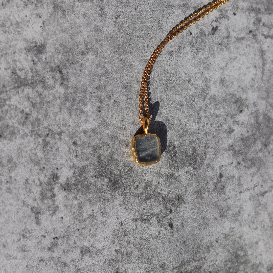 Photo of grey stone gold plated necklace on a grey marble effect background.