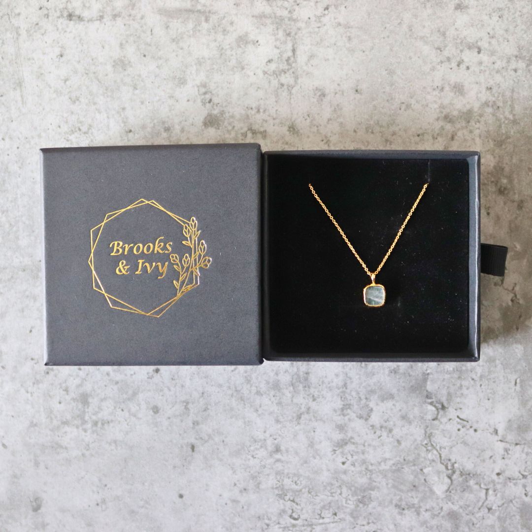 Photo of grey stone gold plated necklace inside gift box on a grey marble effect background.